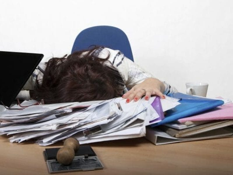 Young female office worker sleep at a desk with a pile of papers
