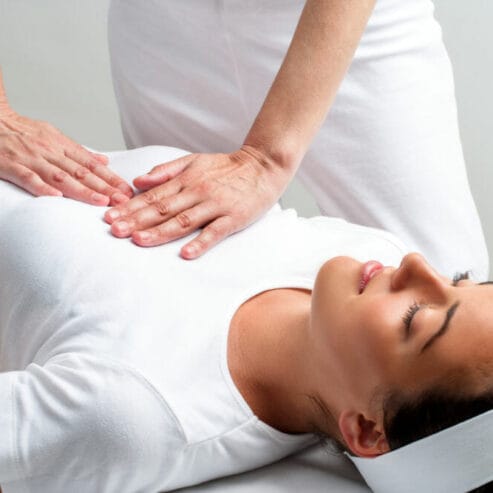 Close up of chiropractor pressing with hands on womans chest at reiki session.